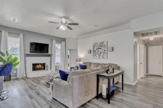 living room with ceiling fan, a fireplace, a textured ceiling, and light hardwood / wood-style flooring