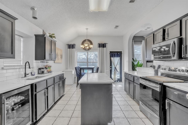 kitchen with appliances with stainless steel finishes, lofted ceiling, sink, beverage cooler, and a center island