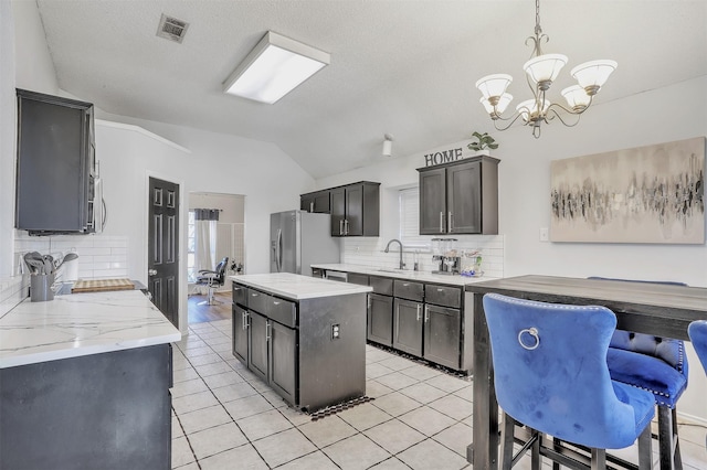 kitchen with tasteful backsplash, vaulted ceiling, appliances with stainless steel finishes, a kitchen island, and pendant lighting