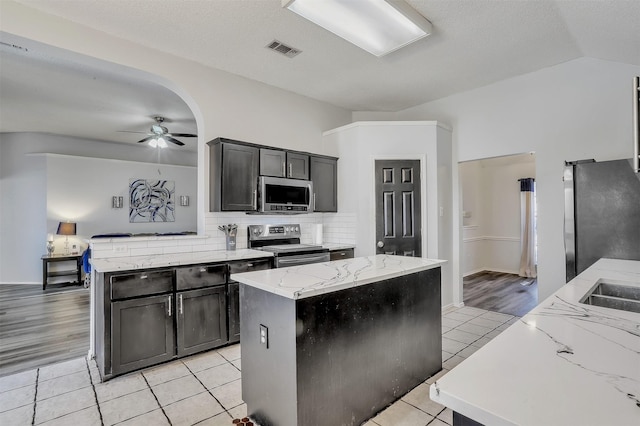 kitchen featuring appliances with stainless steel finishes, a center island, light tile patterned floors, and light stone counters