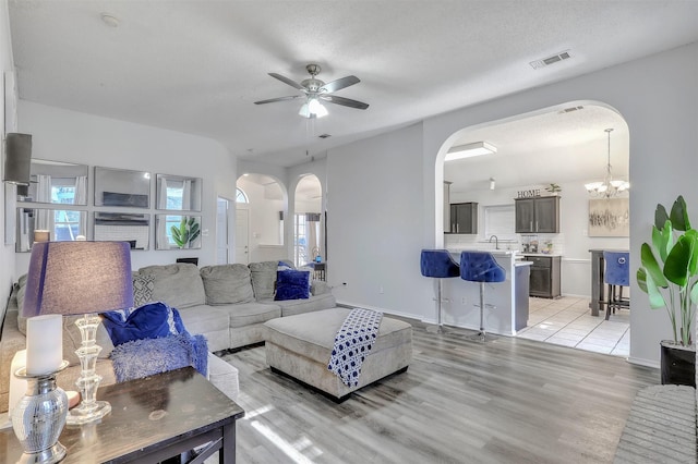 living room with ceiling fan with notable chandelier, a textured ceiling, and light wood-type flooring