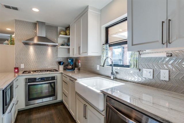 kitchen featuring light stone counters, wall chimney range hood, stainless steel appliances, and white cabinets