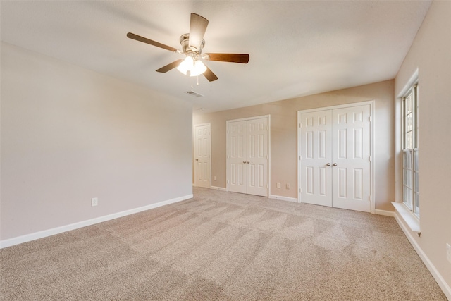 unfurnished bedroom featuring multiple closets, light carpet, and ceiling fan