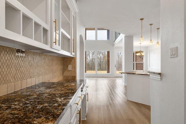 kitchen featuring light hardwood / wood-style flooring, dark stone countertops, decorative backsplash, white cabinets, and decorative light fixtures