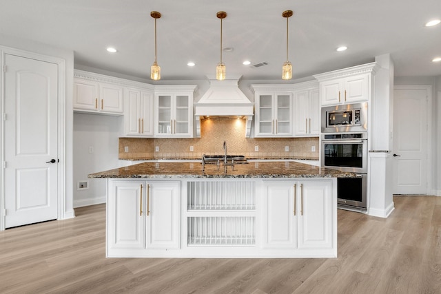 kitchen with premium range hood, white cabinetry, dark stone counters, and hanging light fixtures