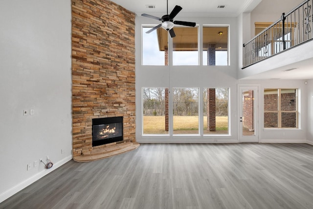 unfurnished living room with ceiling fan, wood-type flooring, a stone fireplace, and a towering ceiling