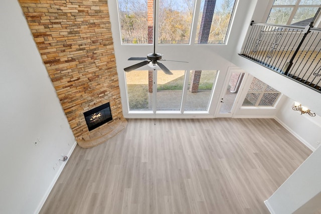 unfurnished living room with light hardwood / wood-style flooring, a fireplace, ceiling fan, and a high ceiling