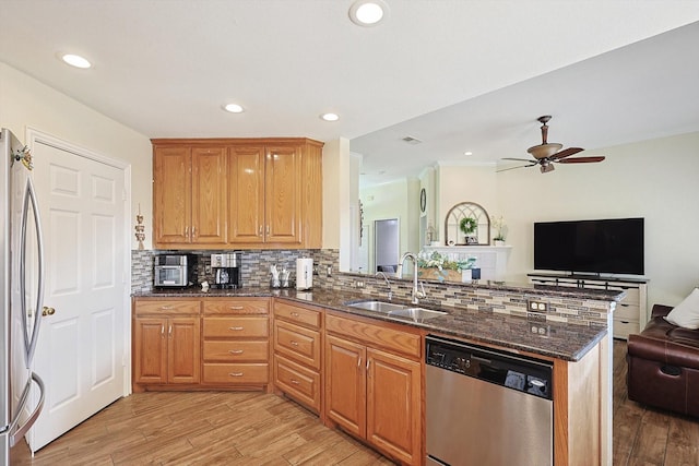 kitchen with sink, dark stone countertops, kitchen peninsula, stainless steel appliances, and backsplash