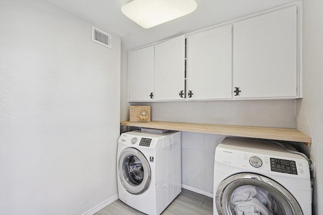 washroom with washing machine and dryer, cabinet space, visible vents, and baseboards