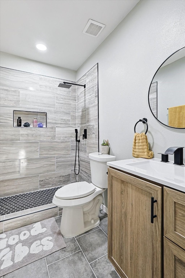 bathroom with vanity, tile patterned flooring, toilet, and tiled shower