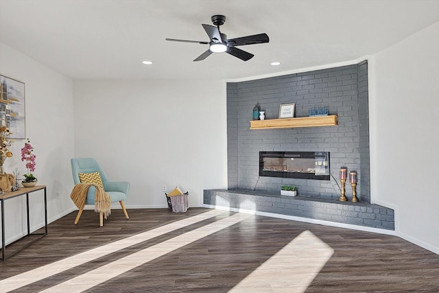 living area with ceiling fan, dark wood-type flooring, and a fireplace