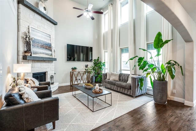 living room featuring hardwood / wood-style flooring, a stone fireplace, a high ceiling, and ceiling fan