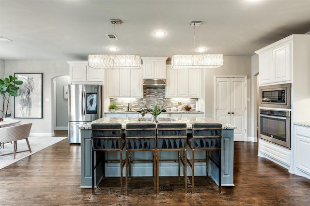 kitchen featuring appliances with stainless steel finishes, light stone countertops, a kitchen island with sink, and hanging light fixtures