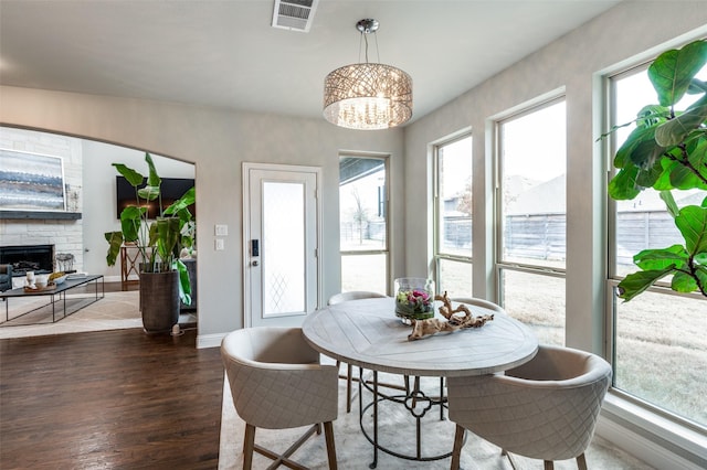 dining space with dark hardwood / wood-style flooring, a healthy amount of sunlight, a chandelier, and a fireplace