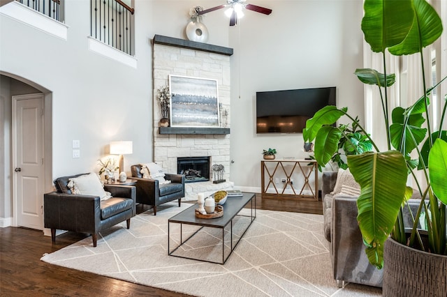 living room with a stone fireplace, a towering ceiling, hardwood / wood-style floors, and ceiling fan