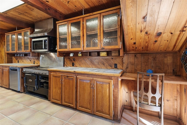 kitchen with light tile patterned flooring, tile countertops, wooden walls, beamed ceiling, and stove