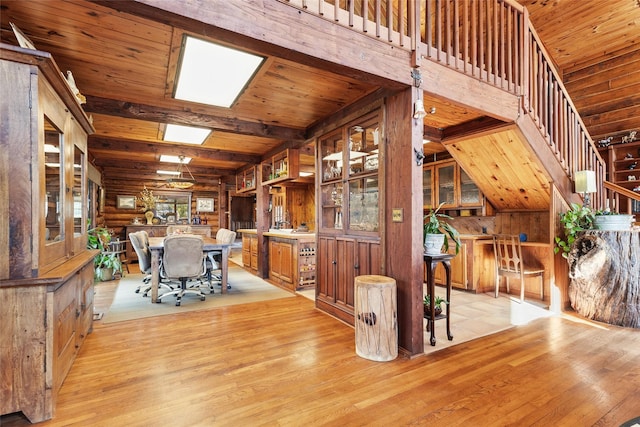 unfurnished dining area with a skylight, wooden walls, light hardwood / wood-style floors, wooden ceiling, and beamed ceiling