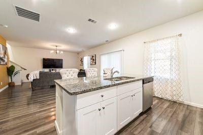 kitchen with sink, white cabinetry, dark stone countertops, dishwasher, and an island with sink