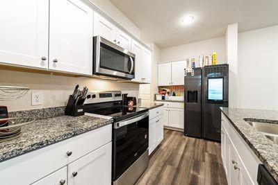 kitchen with light stone countertops, white cabinetry, appliances with stainless steel finishes, and dark wood-type flooring