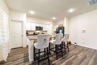 kitchen with dark wood-type flooring, stainless steel appliances, a breakfast bar area, and white cabinets