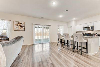 kitchen with a kitchen bar, a kitchen island, stainless steel appliances, light hardwood / wood-style floors, and white cabinets