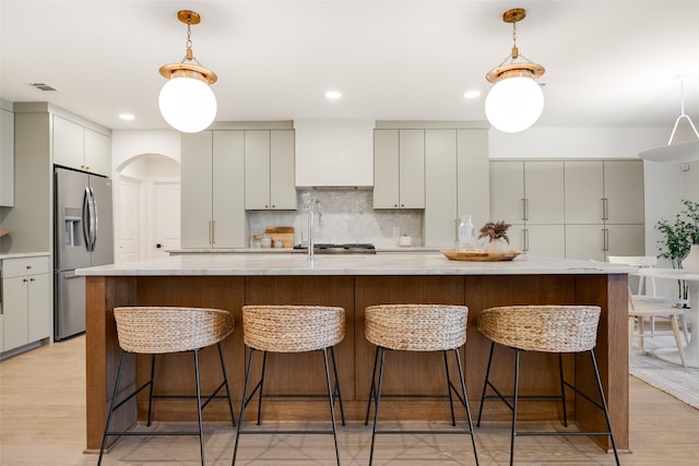 kitchen featuring pendant lighting, backsplash, stainless steel fridge with ice dispenser, and wall chimney range hood