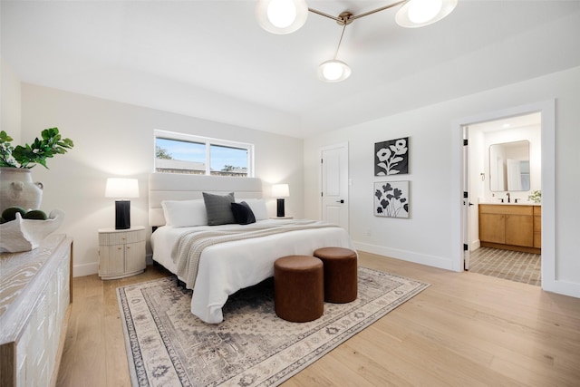 bedroom featuring connected bathroom, sink, and light hardwood / wood-style flooring