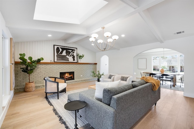 living room featuring lofted ceiling with beams, a brick fireplace, and light wood-type flooring