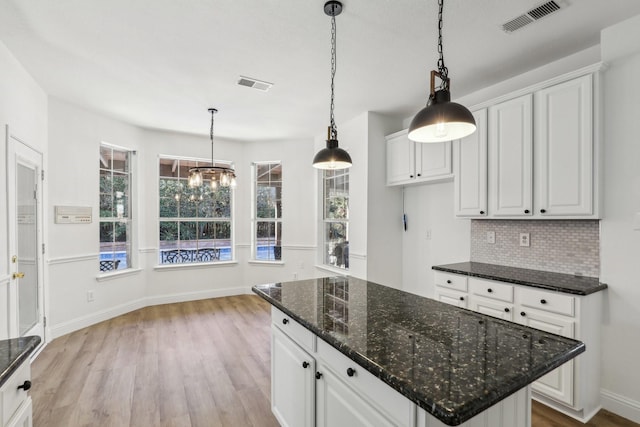 kitchen featuring white cabinetry, decorative light fixtures, and dark stone countertops