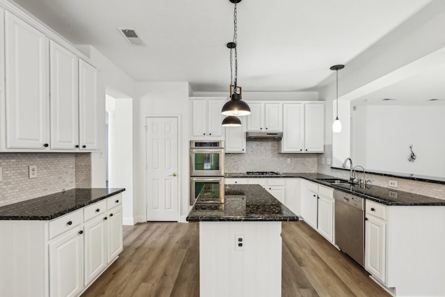 kitchen with decorative light fixtures, dark stone countertops, white cabinets, a center island, and stainless steel appliances