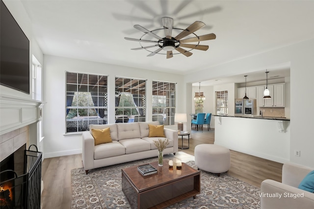 living room featuring ceiling fan, wood-type flooring, a tile fireplace, and a wealth of natural light