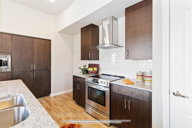 kitchen with light stone counters, wall chimney range hood, decorative backsplash, and stainless steel appliances