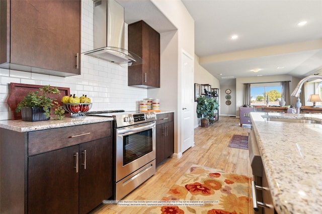 kitchen with light stone counters, wall chimney range hood, vaulted ceiling, and stainless steel range with electric cooktop