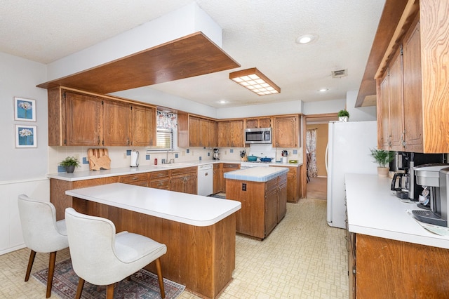 kitchen with a kitchen island, sink, a breakfast bar area, white appliances, and a textured ceiling