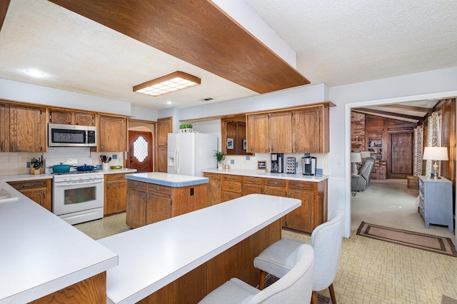 kitchen featuring white appliances, a breakfast bar, a center island, a textured ceiling, and kitchen peninsula