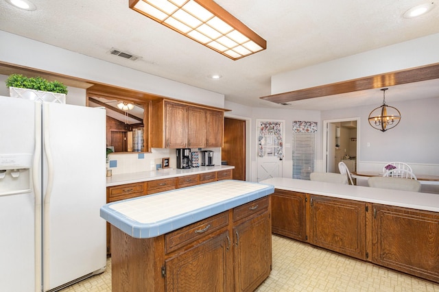 kitchen with hanging light fixtures, tile counters, white refrigerator with ice dispenser, a kitchen island, and a chandelier