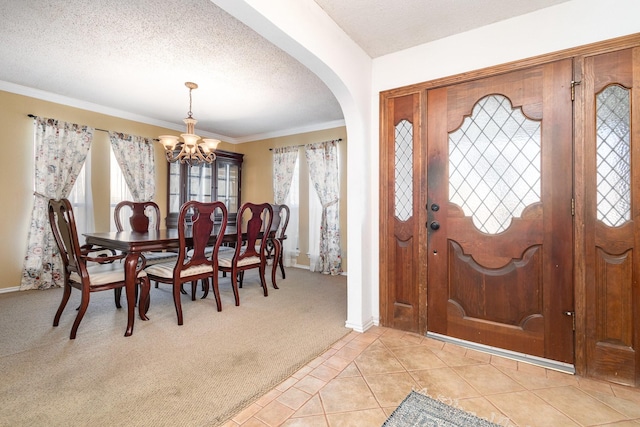 carpeted foyer entrance featuring ornamental molding, a chandelier, and a textured ceiling