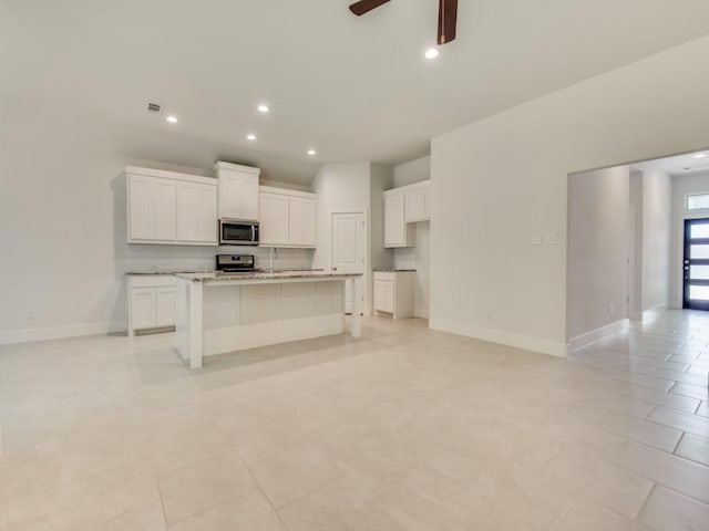 kitchen featuring white cabinetry, stainless steel appliances, an island with sink, and tasteful backsplash