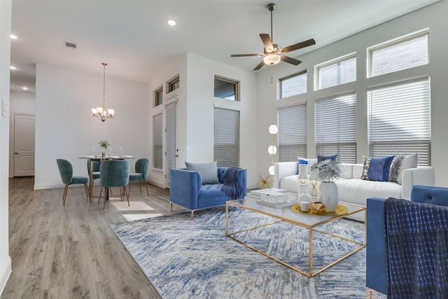 living room featuring wood-type flooring, ceiling fan with notable chandelier, and a high ceiling