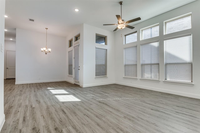 unfurnished living room with a towering ceiling, ceiling fan with notable chandelier, and light hardwood / wood-style flooring