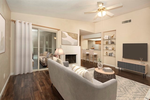 living room with a fireplace, lofted ceiling, dark hardwood / wood-style flooring, ceiling fan, and built in shelves