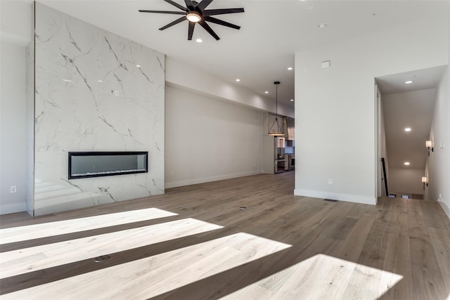 unfurnished living room with a ceiling fan, wood finished floors, baseboards, a premium fireplace, and recessed lighting