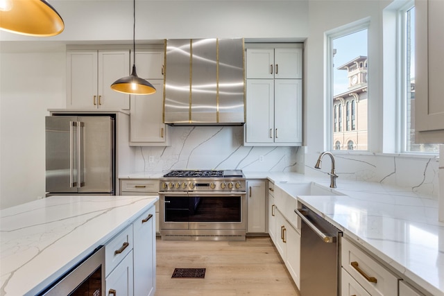 kitchen featuring ventilation hood, light wood-style flooring, a sink, decorative backsplash, and premium appliances