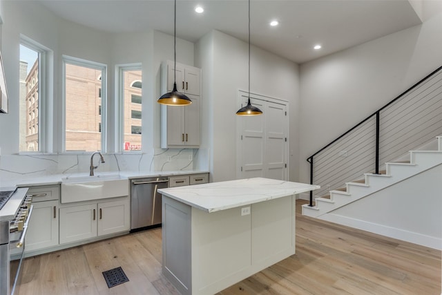 kitchen with dishwasher, light stone countertops, light wood-style floors, and a sink