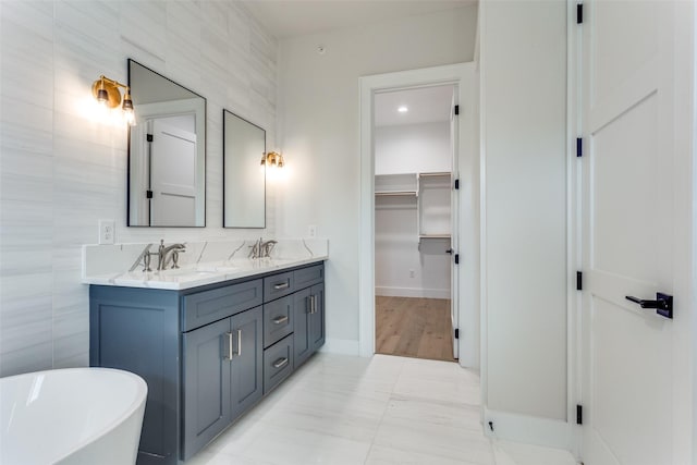 full bathroom with double vanity, a freestanding tub, tile walls, and a sink