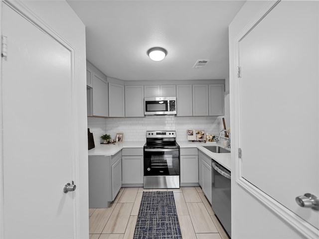 kitchen featuring stainless steel appliances, tasteful backsplash, sink, and gray cabinetry