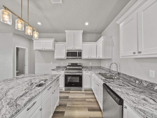 kitchen featuring appliances with stainless steel finishes, sink, white cabinets, hanging light fixtures, and light wood-type flooring