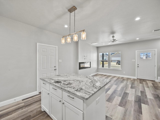 kitchen featuring light stone counters, decorative light fixtures, a center island, light hardwood / wood-style flooring, and white cabinets