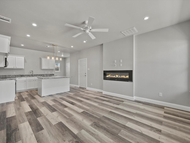 unfurnished living room with ceiling fan, sink, and light wood-type flooring