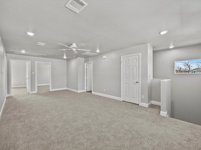 basement featuring light carpet, ceiling fan, and a textured ceiling